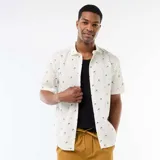 Camisa de manga corta color blanco con diseño estampado de pequeñas palmeras negras, cuello camisero y cierre frontal de botones.