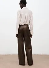 Pantalón wide leg de efecto piel color marrón, con tiro medio, bolsillos laterales, pinzas delanteras y cierre frontal con botón, gancho y cremallera ocultos. Cuenta con forro interior.