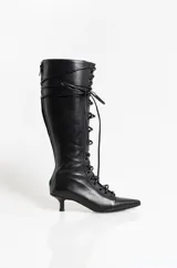 Bota alta de cuero negro con cordones frontales, punta fina y taco bajo tipo kitten heel. Presenta un diseño estilizado con cierre lateral.