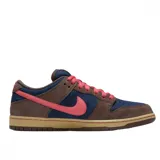 Championes Nike SB Dunk Low con diseño de paneles en gamuza azul marino y marrón, destacando el swoosh lateral y los cordones en color rosa. Presenta una suela de goma en tono tostado.