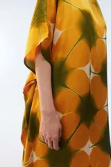 Kaftan maxi amplio de color amarillo, con escote redondo, mangas cortas y ruedo irregular. Presenta un diseño estampado a cuadros con efecto teñido.