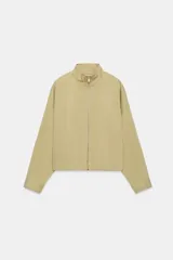 Cazadora bomber de color beige con cuello subido, manga larga y bolsillos delanteros. Cuenta con cierre frontal de cremallera metálica y cordón ajustable en el dobladillo.