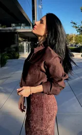 Camisa de gamuza color marrón, con cuello clásico, cierre frontal de botones y bolsillos delanteros tipo parche.