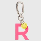 Llavero con dije en forma de letra A color rosado y pequeño dije circular amarillo con logo de la marca grabado. Incluye gancho metálico tipo mosquetón.