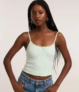 Blusa de breteles finos confeccionada en poliamida seamless texturizada de color verde menta, con escote redondo adornado con encaje y una pequeña moña al frente.