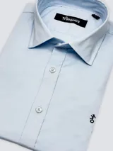 Camisa de hombre de corte clásico con cuello italiano, confeccionada en 100% algodón. Presenta un diseño de cuadros pequeños en azul y blanco, con cierre frontal de botones y logo bordado en el pecho.