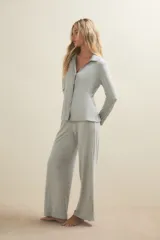 Conjunto de pijama compuesto por una camisa de manga larga con cuello solapa y cierre frontal de botones, y un pantalón de corte recto. Ambas prendas están confeccionadas en tejido de punto acanalado de color gris claro.