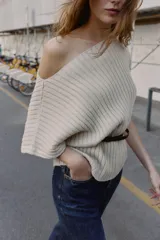 Top de punto rib color beige claro, con escote barco y mangas cortas asimétricas. Se ajusta a la cintura con un cinturón fino negro con hebilla metálica.