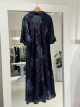 Vestido largo color azul marino con estampado floral en tonos violeta y bordó, estilo camisero con cuello tipo solapa, cierre frontal parcial con botones y mangas largas remangables.