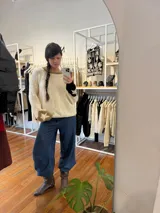 Buzo de tejido de punto artesanal en lana merino color crema, con diseño de estilo cowboy en la espalda que muestra una figura a caballo. Presenta detalles en color rojo en el cuello y en los puños de las mangas.