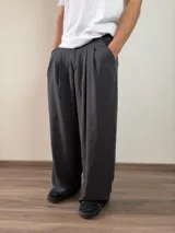 Pantalón de vestir de corte baggy, color gris oscuro, con pinzas frontales y bolsillos laterales.