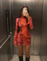 Vestido corto de microtul elastizado con estampado psicodélico en tonos rosado, rojo y naranja, cuello alto y mangas largas acampanadas.