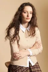 Cardigan de tejido de punto fino en color beige, con cuello redondo, cierre frontal con botones y mangas largas.