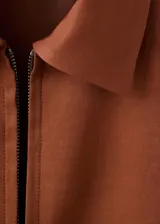 Chaqueta color marrón terracota de cuello camisero, manga larga, bolsillos laterales y cierre frontal con cremallera.