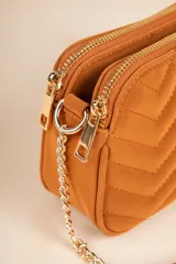 Bandolera negra con diseño acolchado en forma de zigzag, correa de cadena plateada y correa de cuero sintético ajustable.