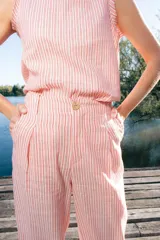 Pantalón de lino de corte sastrero, tiro medio y pierna recta con pinzas. Diseño a rayas blancas y rojas, con bolsillos laterales y botón frontal efecto madera.