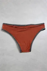Bottom de bikini color marrón con detalles estampados a cuadros en las terminaciones y placa metálica con logo en la cintura.