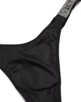 Panty tipo tanga negra con tiras laterales brillantes decoradas con pedrería y la inscripción de la marca Victoria's Secret.