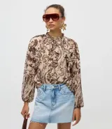 Blusa de chiffon con estampado paisley en tonos tierra, cuello alto con lazo frontal, volados decorativos y mangas largas con puños ajustados.