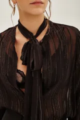 Camisa de transparencia con diseño a rayas verticales, cuello con lazo integrado y mangas largas abullonadas con puños ajustados.