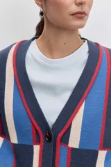 Cardigan de punto con diseño de bloques de color en azul, rojo y crema. Presenta cuello en V, cierre frontal con botones, mangas largas y dos bolsillos delanteros con bordado de cerezas.
