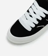 Championes de estilo skater para hombre, confeccionados en poliuretano color marrón oscuro. Poseen punta redonda, caña baja y suela de plataforma blanca. Destacan por sus cordones anchos tipo fat lace y detalles laterales en contraste.
