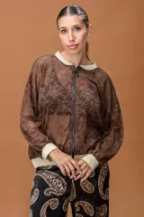 Campera tipo bomber confeccionada en encaje color marrón, con cierre frontal completo. Presenta cuello, puños y ruedo en tejido elástico con acabado brillante en tono dorado.