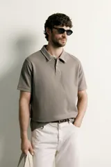 Remera polo regular fit de color gris oscuro, confeccionada en tejido de algodón con textura de rayas verticales. Cuenta con cuello solapa, cierre frontal con botones y mangas cortas con terminación en rib.
