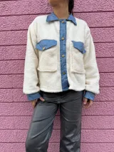 Chaqueta color crema de corderito con detalles en jean azul en cuello, solapa, bolsillos y puños.