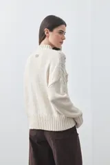 Polera de tejido de punto color marrón, con cuello alto y diseño de textura con relieves y trenzas. Posee mangas largas con puños acanalados.