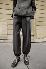 Pantalón de tiro alto confeccionado en material con efecto piel, con cintura elástica, bolsillos delanteros y nervio marcado en el frente. Presenta un diseño bombacho con bajo ajustable mediante cordones elásticos.