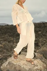 Pantalón de organza color crudo, de corte holgado y diseño traslúcido. Presenta cintura elástica con cordón ajustable y terminaciones en los tobillos con tancas metálicas.