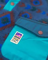 Buzo de polar fleece con diseño estampado geométrico en tonos azules, bordó y verde. Presenta cuello alto con cierre de botones a presión, bolsillo frontal con solapa en contraste y puños elásticos.