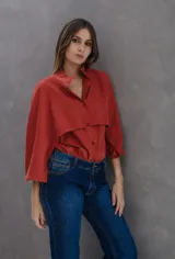 Camisa de seda peletizada color ladrillo con diseño de capa superpuesta. Presenta cuello mao, mangas bombé y cierre frontal con botones al tono.