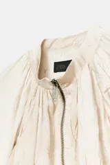 Cazadora de cuello redondo y manga larga, confeccionada con acabado efecto arrugado y cierre frontal con cremallera metálica. Presenta bolsillos en el delantero y diseño fluido con bajo ajustable.