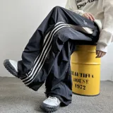 Pantalón deportivo negro de corte ancho con cintura elástica ajustable, bolsillos laterales y tres rayas blancas verticales en los laterales.