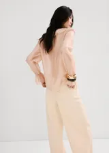 Blusa de seda color rosa pálido con volados frontales, cuello redondo y mangas largas con puños elásticos.