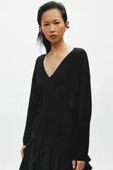 Jersey de punto fino negro con escote en V pronunciado, mangas largas y corte holgado con bajo asimétrico, más largo en la parte trasera.