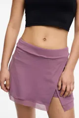 Falda short deportiva color violeta, con calza interna y bolsillo lateral. Presenta un frente cruzado y detalle de microtul en el dobladillo.