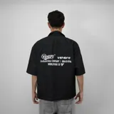 Camisa negra de corte oversize, manga corta y cuello tipo bowling. Presenta botones frontales y estampado con el logo de la marca en el pecho.