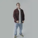 Campera color borgoña de pana con cuello camisero, cierre frontal con botones a presión y dos bolsillos de parche en el pecho. Interior acolchado con patrón de rombos.