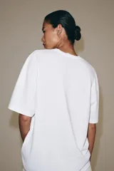 Camiseta blanca de manga corta y cuello redondo, de corte regular fit, con detalle de texto estampado en negro en el frente.