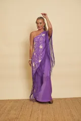 Vestido largo morado de un solo hombro, con detalles bordados florales en tono crudo y un gran mantón con flecos largos del mismo color.
