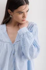 Camisa color crema de algodón con bordado calado, escote en V y mangas largas abullonadas.