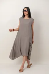 Vestido midi de lino color beige, sin mangas y con cuello redondo. Cuenta con un diseño irregular con detalle de volado vertical a un costado.