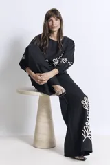 Pantalón negro de corte palazzo con bolsillos laterales y apliques bordados de hojas en color crudo en una pierna.