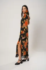 Vestido largo negro con estampado de flores naranjas y amarillas, cuello mao con abertura en forma de gota, mangas largas acampanadas con botones en los puños, tajo lateral y flecos en el ruedo.