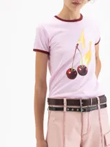 Remera de algodón pima orgánico color marrón, con cuello redondo y bordes de mangas en color rosa. Presenta un estampado frontal de cerezas con llamas.