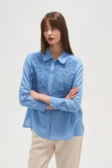 Camisa de manga larga color celeste, con cuello camisero y cierre frontal de botones. Presenta un diseño distintivo con paneles de encaje tipo crochet en la parte superior delantera.
