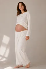Conjunto de pijama compuesto por una remera de manga larga con detalle de bordado en el pecho y un pantalón de corte holgado. Ambas prendas presentan terminaciones con encaje en los bordes.
